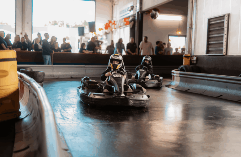 Mehrere Karts fahren in einer Kurve im Wettkampf beim Kartcenter Cologne, Zuschauer verfolgen das Kartfahren Köln.